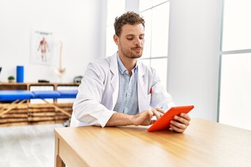 Sticker - Young hispanic man wearing physiotherapist uniform using touchpad at clinic