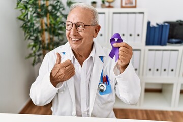 Sticker - Senior doctor man holding purple ribbon awareness pointing thumb up to the side smiling happy with open mouth