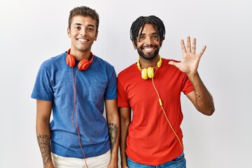 Canvas Print - Young hispanic brothers standing over isolated background wearing headphones showing and pointing up with fingers number five while smiling confident and happy.