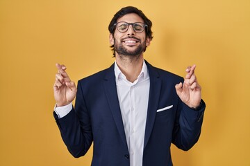 Sticker - Handsome latin man standing over yellow background gesturing finger crossed smiling with hope and eyes closed. luck and superstitious concept.