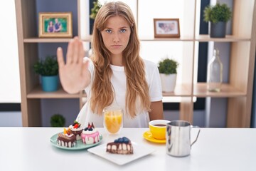 Wall Mural - Young caucasian woman eating pastries t for breakfast doing stop sing with palm of the hand. warning expression with negative and serious gesture on the face.