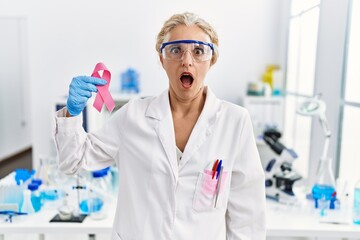 Poster - Middle age blonde woman working at laboratory looking for breast cancer cure scared and amazed with open mouth for surprise, disbelief face