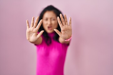 Wall Mural - Young asian woman standing over pink background doing stop gesture with hands palms, angry and frustration expression