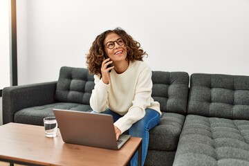 Sticker - Middle age hispanic woman using laptop talking on the smartphone at home