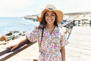 Poster - Young latin girl smiling happy wearing summer hat at the beach.