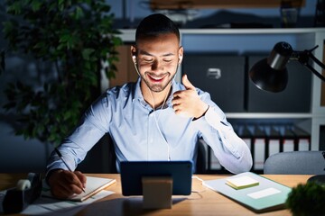 Poster - Young hispanic man working at the office at night doing happy thumbs up gesture with hand. approving expression looking at the camera showing success.