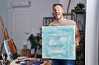 © Krakenimages.com - Young hispanic painter man holding canvas smiling and laughing hard out loud because funny crazy joke.