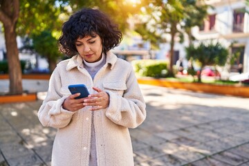 Young beautiful hispanic woman using smartphone with serious expression at park