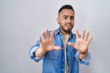 Canvas Print - Young hispanic man standing over isolated background afraid and terrified with fear expression stop gesture with hands, shouting in shock. panic concept.