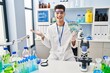 © Krakenimages.com - Young hispanic man working at scientist laboratory holding brazilian reals celebrating achievement with happy smile and winner expression with raised hand