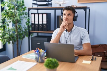 Sticker - Young hispanic man working at the office wearing headphones with hand on chin thinking about question, pensive expression. smiling with thoughtful face. doubt concept.