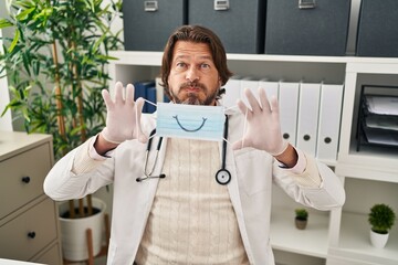 Poster - Handsome middle age doctor man wearing safety mask puffing cheeks with funny face. mouth inflated with air, catching air.