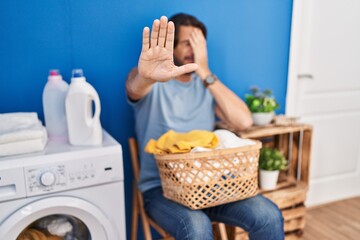 Sticker - Handsome middle age man waiting for laundry covering eyes with hands and doing stop gesture with sad and fear expression. embarrassed and negative concept.