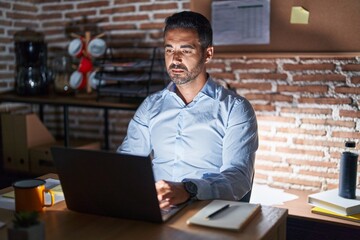 Poster - Hispanic man with beard working at the office at night relaxed with serious expression on face. simple and natural looking at the camera.