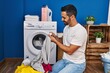 Young hispanic man washing clothes looking t shirt label at laundry room