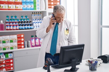 Poster - Middle age grey-haired man pharmacist talking on smartphone using computer at pharmacy