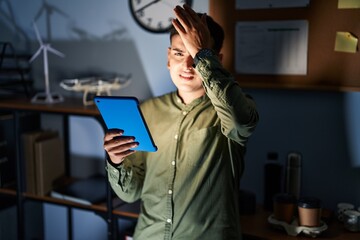 Canvas Print - Non binary person using touchpad device at night surprised with hand on head for mistake, remember error. forgot, bad memory concept.