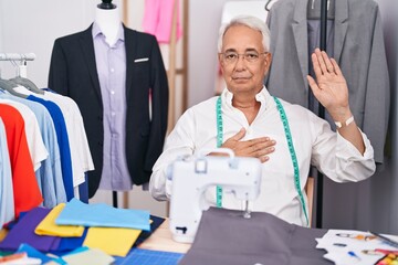 Poster - Middle age man with grey hair dressmaker using sewing machine swearing with hand on chest and open palm, making a loyalty promise oath