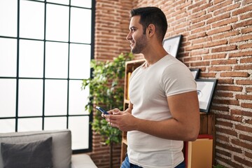 Wall Mural - Young hispanic man smiling confident using smartphone at home