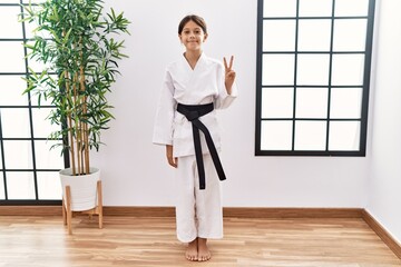 Sticker - Young hispanic girl wearing karate kimono and black belt showing and pointing up with fingers number two while smiling confident and happy.