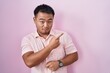 © Krakenimages.com - Chinese young man standing over pink background pointing with hand finger to the side showing advertisement, serious and calm face