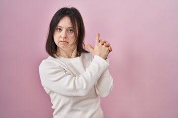 Wall Mural - Woman with down syndrome standing over pink background holding symbolic gun with hand gesture, playing killing shooting weapons, angry face