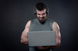 Young bodybuilder, online fitness coach, using a laptop and a headset to talk to an online client, studio image