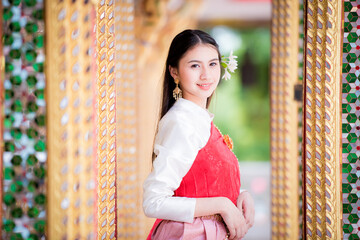 Wall Mural - Portrait of a beautiful woman wearing a traditional Thai dress smiling gracefully standing in a temple of Thailand