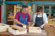 © ND STOCK - A tutor with a Female carpenter student in a workshop studying for an apprenticeship at a college using a tape measure.