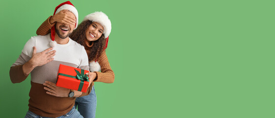 Wall Mural - Young woman giving Christmas present to her husband on green background with space for text