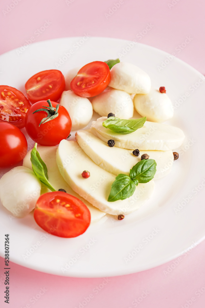 Plate with tasty mozzarella cheese, tomatoes and basil on pink background