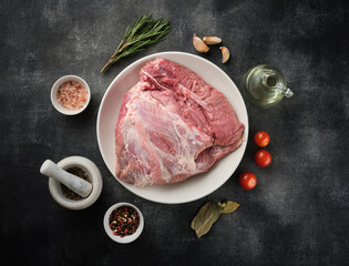 Wall Mural - Fresh raw pork shoulder with ingredients for marinade: pepper, salt, olive oil, rosemary, garlic, view from above, close-up.