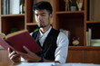 © Jirapong - A portrait of a handsome and discreet Asian man sitting at his desk reading a book