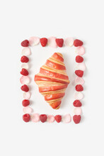 Fresh Croissant Amidst Frame Made Of Raspberries And Rose Petals Against White Background