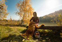 Woman With Yellow Leaves Knitting Scarf On Log At Park