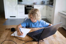 Boy Doing Homework With Laptop On Table At Home