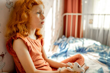 Thoughtful Redhead Girl With Soft Toy Sitting On Bed