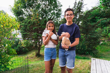 Brother And Sister Holding Rabbits Standing In Back Yard