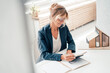 © Westend61 - Smiling businesswoman looking at diary by house model on desk in office
