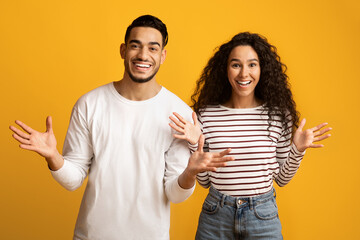 Wall Mural - Portrait Of Joyful Arab Couple Spreading Hands With Excitement Over Yellow Background