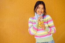 Smiling Young Woman Standing With Orange Juice In Front Of Wall