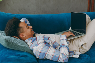 Sticker - Side view young IT man in casual shirt lay down on blue sofa couch hold use work on laptop pc computer blank screen stay at home flat rest relax spend free spare time in living room indoor grey wall