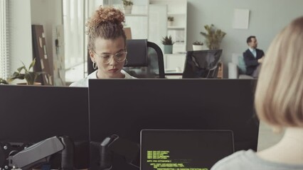 Young Caucasian woman working on computer in bright modern IT office with diverse colleagues