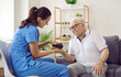 © Studio Romantic - Friendly smiling nurse or physiatrist holding spiky prickly texture rubber ball and doing hand massage to senior man sitting on couch in retirement home. Old age, health, physiotherapy concept