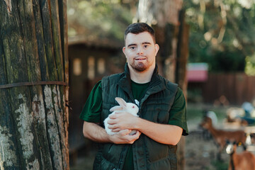 Caretaker with down syndrome taking care of animals in zoo, stroking rabbit. Concept of integration people with disabilities into society.