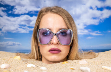 Wall Mural - Woman buried in sand on beach with sunglasses