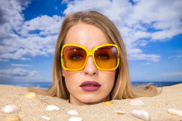 Wall Mural - Woman buried in sand on beach with sunglasses