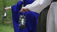 Women In Medieval Dresses With Lanterns Walk Through Wood