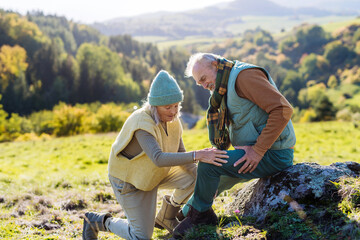 Wall Mural - Senior man with hurting knee resting during autumn walk, his wife taking care of him.