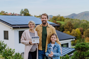 Wall Mural - Happy family holding paper model of house with solar panels.Alternative energy, saving resources and sustainable lifestyle concept.